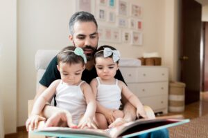 A mid adult latin father reading a book to his baby twin daugthers at home in a horizontal medium shot indoors. (A mid adult latin father reading a book to his baby twin daugthers at home in a horizontal medium shot indoors., ASCII, 112 components, 11